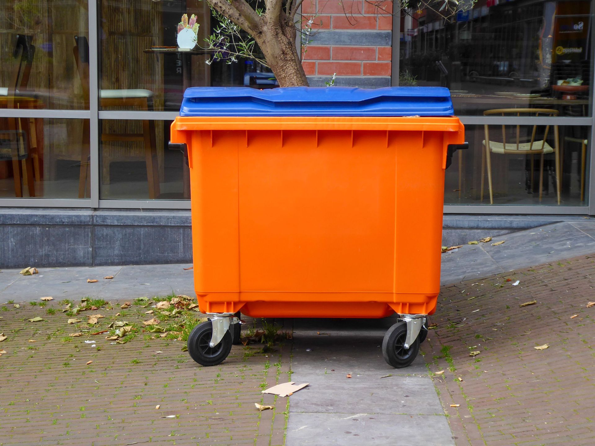 Vibrant orange bin with blue lid situated outside urban building, capturing urban waste management theme.